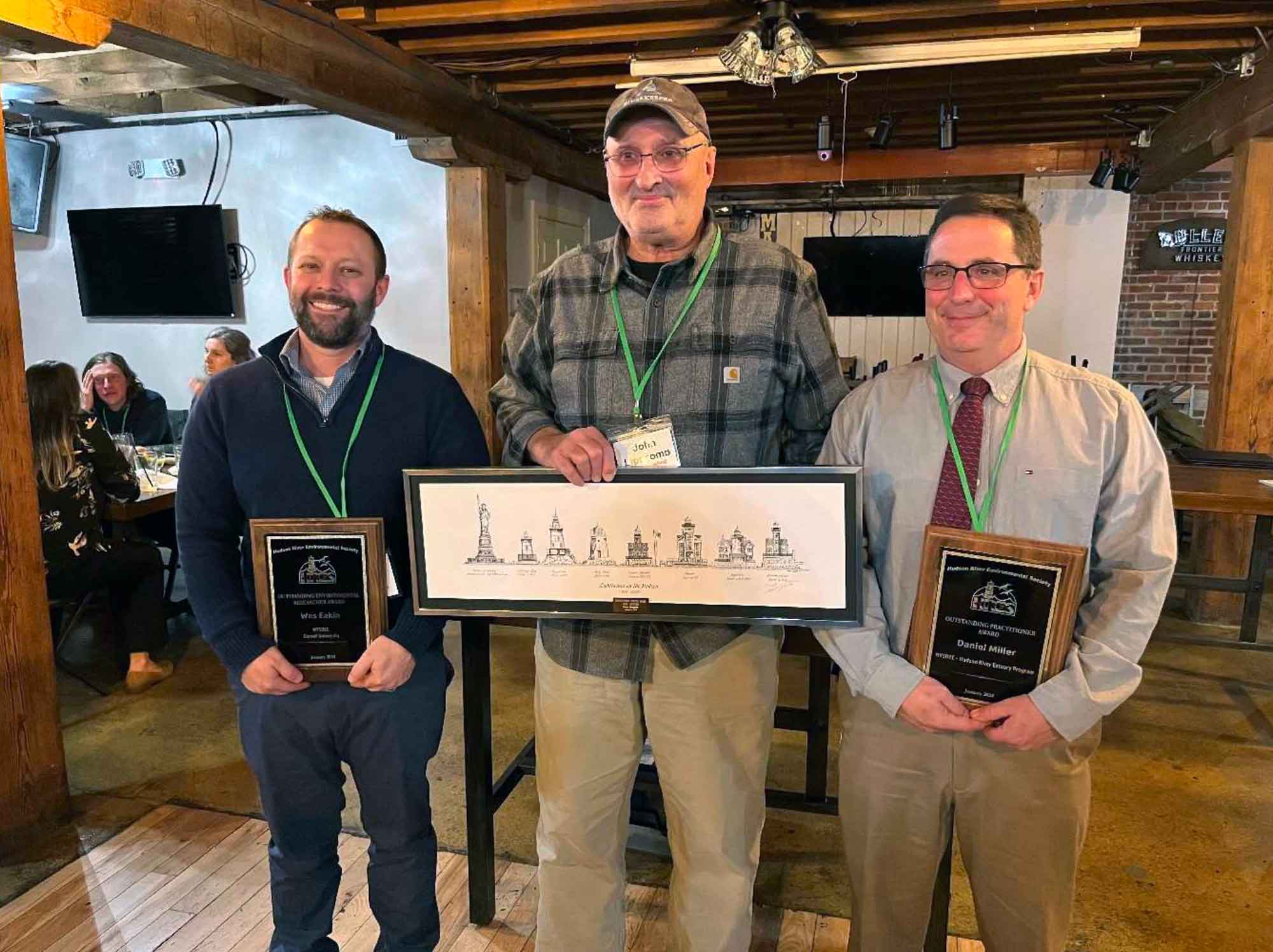 Three smiling people standing and holding awards.